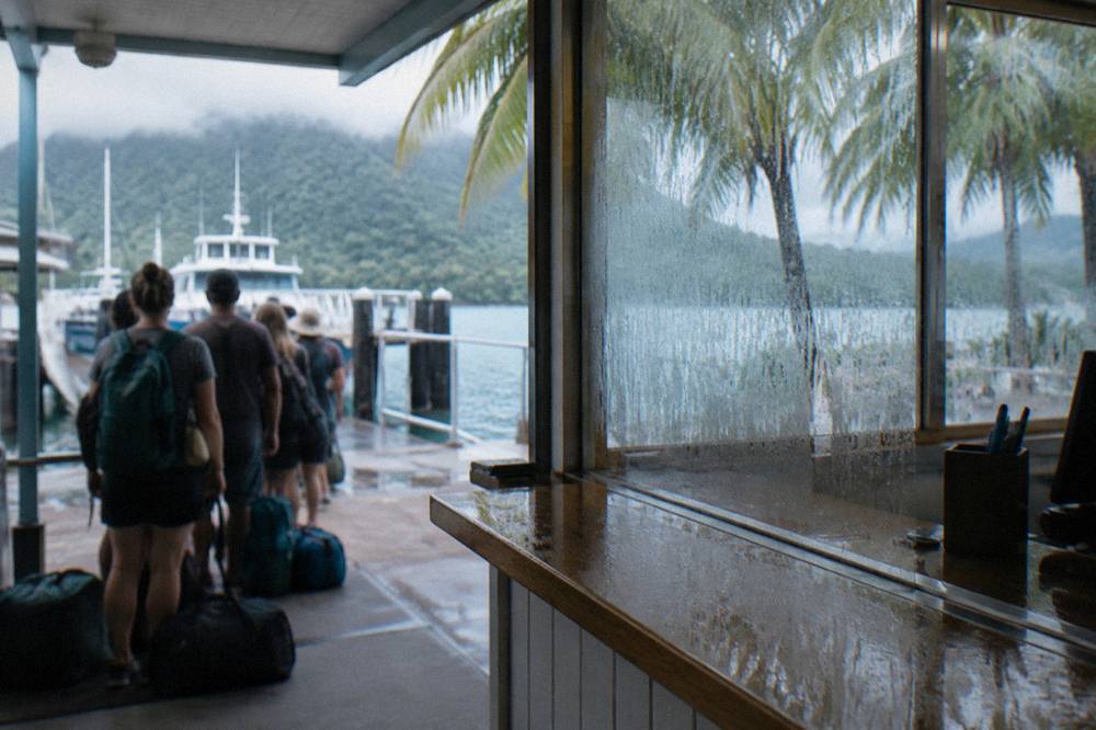 A ferry terminal counter queue of travellers with day packs waiting at a marina check-in desk