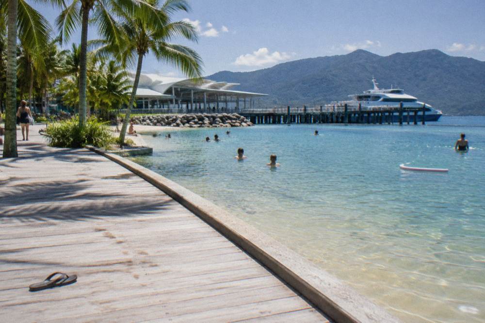 Waterfront promenade in Cairns beside a lagoon swimming area with palm trees